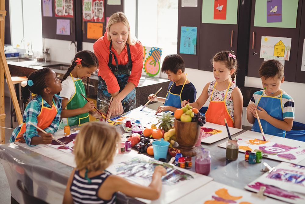 Teacher assisting schoolkids in drawing class at a Preschool & Daycare Serving New Braunfels, TX