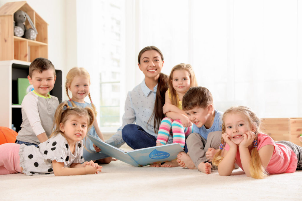 Kindergarten teacher reading book to children indoors at a Preschool & Daycare Serving New Braunfels, TX